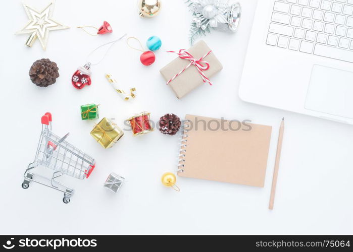 Shopping cart and Christmas decorations on white background with laptop computer and empty notebook, Top view