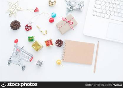 Shopping cart and Christmas decorations on white background with laptop computer and empty notebook, Top view