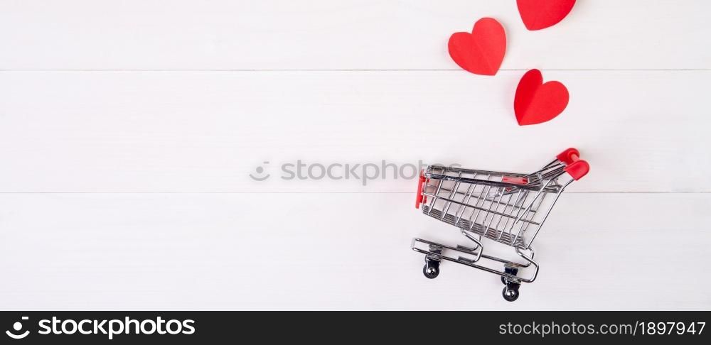 Shopping cart and heart shape paper on wooden table, sale concept in festive valentine day February 14, supermarket and store, symbol and celebration, commerce and selling in holiday concept.