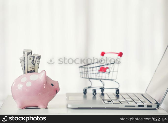 shopping cart and piggy bank with laptop on the desk, online shopping concept