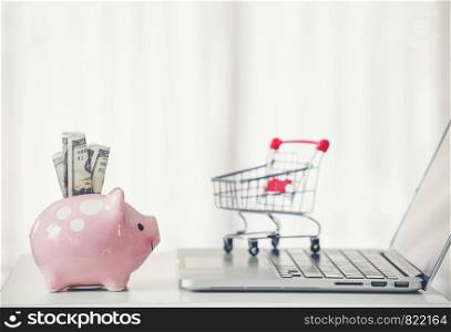 shopping cart and piggy bank with laptop on the desk, online shopping concept