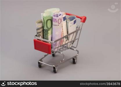 shopping cart full of euro banknotes isolated on gray background