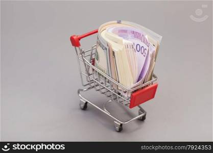 Shopping cart full of money (dollar, euro) isolated on gray background