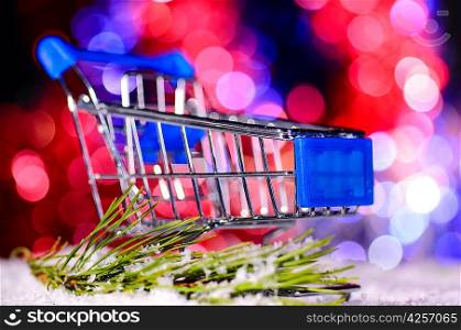 shopping cart on snow against blurred lights on christmas tree