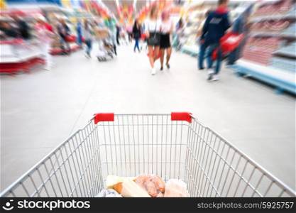 Shopping cart, trolley in a big supermarket with blured people