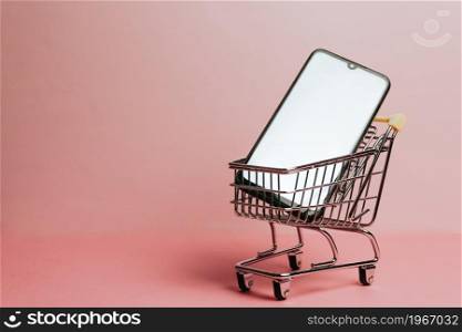Shopping cart with a blank mobile phone over a pastel pink background, e commerce, online buying, online commerce, background, technology, shopping day, black friday and network, copy space, mock up