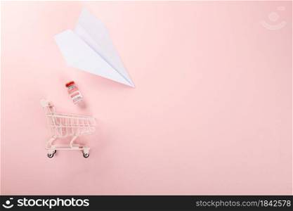 Shopping cart with vaccine vials bottles and syringes for vaccination against coronavirus and paper plane for transportation, medicine illness, COVID-19 disease vaccine isolated on pink background