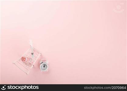 Shopping cart with vaccine vials bottles and syringes for vaccination against coronavirus, medicine illness, COVID-19 disease vaccine isolated on pink background