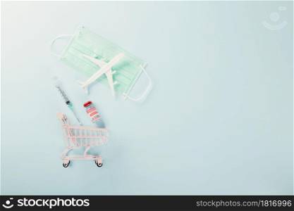 Shopping cart with vaccine vials bottles for vaccination, model plane and medicine face mask vaccine transportation concept, buy vaccine, studio shot isolated blue background with copy space for text