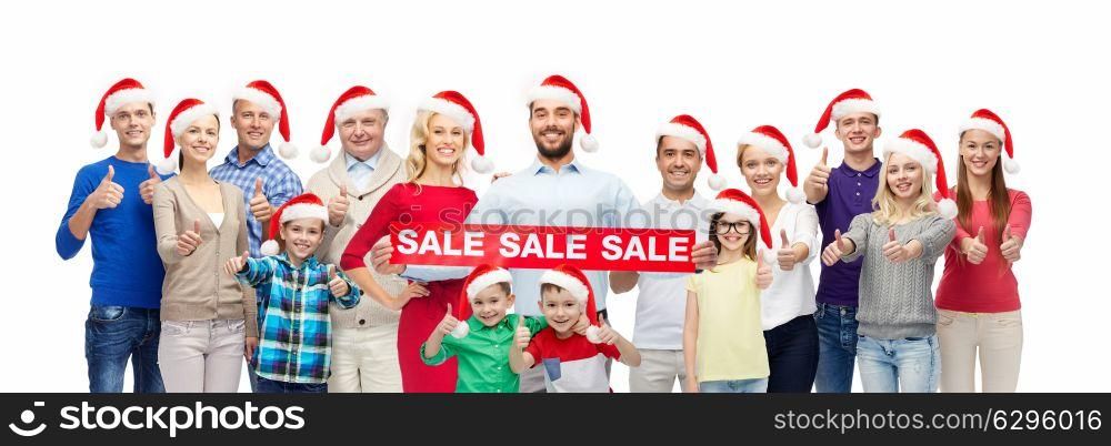 shopping, christmas and holidays concept - group of happy people in santa hats with sale sign showing thumbs up. people in santa hats with sale sign at christmas