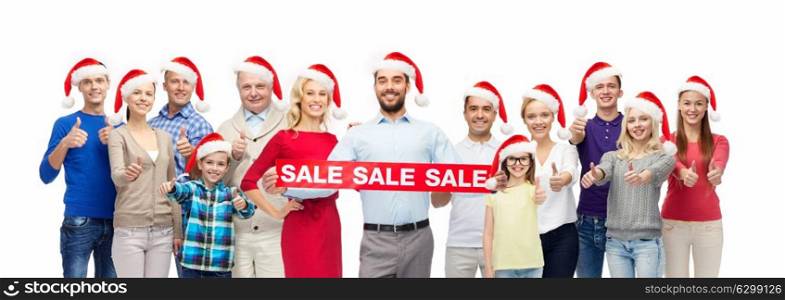 shopping, christmas and holidays concept - group of happy people in santa hats with sale sign showing thumbs up. people in santa hats with sale sign at christmas
