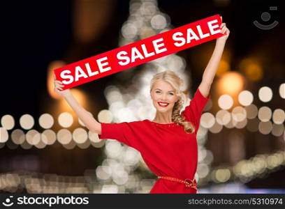 shopping, christmas and people concept - smiling woman in dress with red sale sign over lights background. woman in dress with red sale sign