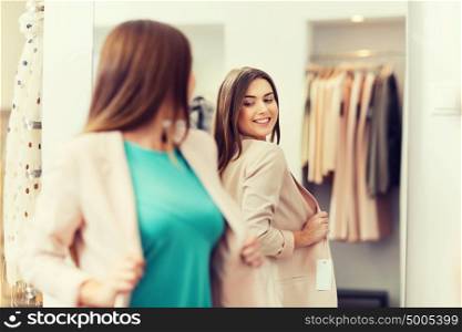 shopping, clothes, fashion, style and people concept - happy woman choosing jacket and posing at mirror in mall or clothing store. happy woman posing at mirror in clothing store