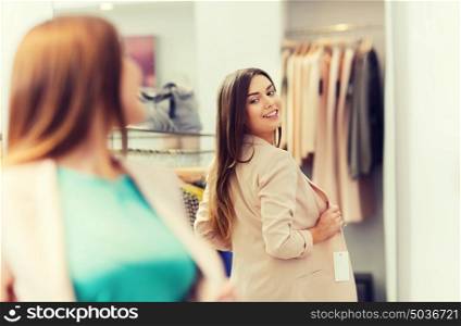 shopping, clothes, fashion, style and people concept - happy woman choosing jacket and posing at mirror in mall or clothing store. happy woman posing at mirror in clothing store