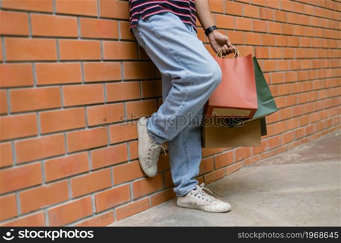 shopping concept A person in light blue jeans and white shoes leaning on the wall of the building while holding a lot of paper shopping bags.