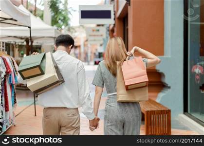 shopping concept Both male and female shoppers holding each other&rsquo;s hand and carrying shopping bags on each back while walking past clothes shop.