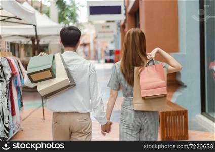 shopping concept Both male and female shoppers holding each other&rsquo;s hand and carrying shopping bags on each back while walking past clothes shop.