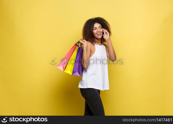 Shopping Concept - Close up Portrait young beautiful attractive African woman smiling and joyful with colorful shopping bag. Yellow Pastel wall Background. Copy Space. Shopping Concept - Close up Portrait young beautiful attractive African woman smiling and joyful with colorful shopping bag. Yellow Pastel wall Background. Copy Space.