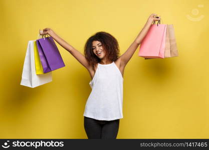 Shopping Concept - Close up Portrait young beautiful attractive African woman smiling and joyful with colorful shopping bag. Yellow Pastel wall Background. Copy Space. Shopping Concept - Close up Portrait young beautiful attractive African woman smiling and joyful with colorful shopping bag. Yellow Pastel wall Background. Copy Space.
