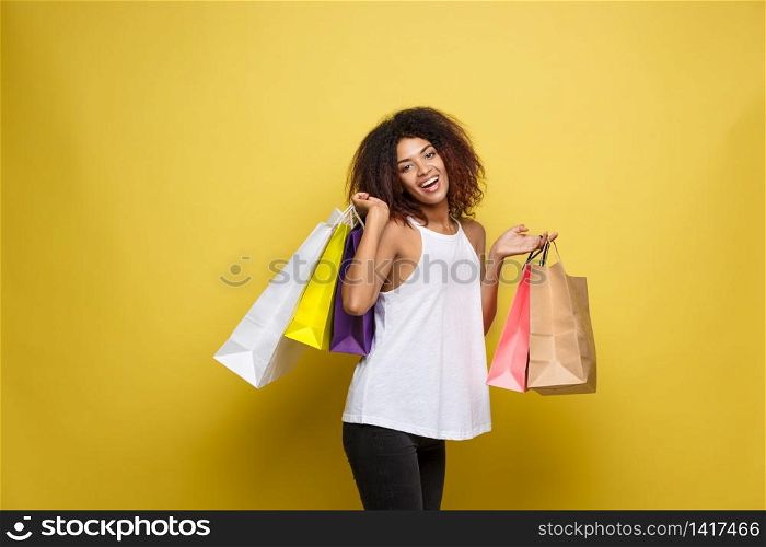 Shopping Concept - Close up Portrait young beautiful attractive African woman smiling and joyful with colorful shopping bag. Yellow Pastel wall Background. Copy Space. Shopping Concept - Close up Portrait young beautiful attractive African woman smiling and joyful with colorful shopping bag. Yellow Pastel wall Background. Copy Space.