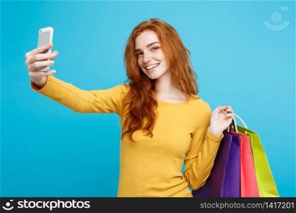 Shopping Concept - Close up Portrait young beautiful attractive redhair girl smiling looking at camera with white shopping bag and selfie. Blue Pastel Background. Copy space.