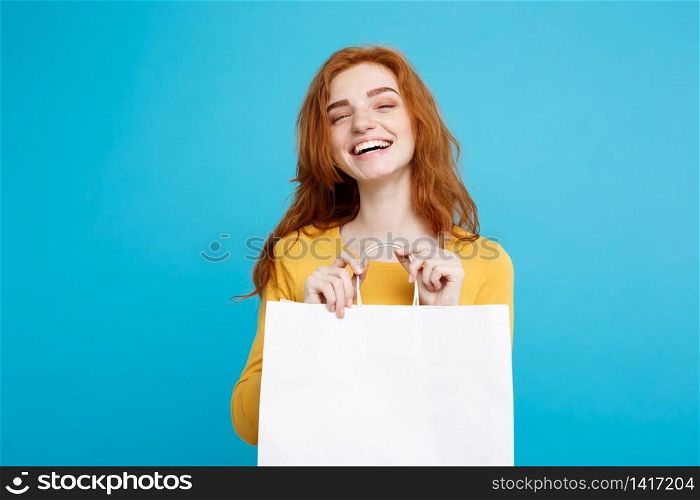Shopping Concept - Close up Portrait young beautiful attractive redhair girl smiling looking at camera with white shopping bag. Blue Pastel Background. Copy space.