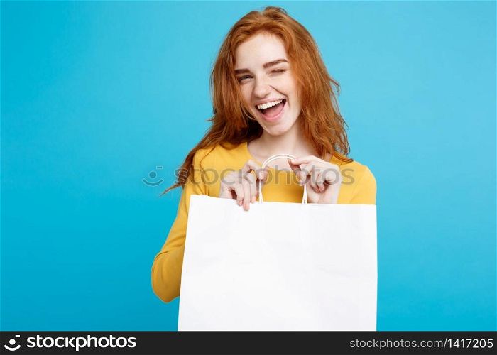 Shopping Concept - Close up Portrait young beautiful attractive redhair girl smiling looking at camera with white shopping bag. Blue Pastel Background. Copy space.