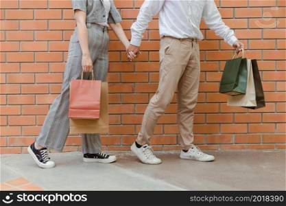 shopping concept The man in light brown pants and white shoes carrying his shopping bag on his left and holding the hand of the woman in grey pants and black shoes.