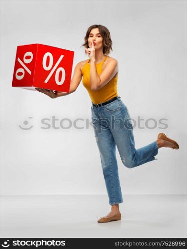shopping, consumerism and people concept - happy smiling young woman in mustard yellow top and jeans with sale sign making hush gesture over grey background. happy smiling young woman with sale sign