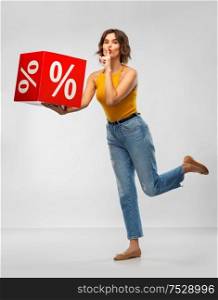 shopping, consumerism and people concept - happy smiling young woman in mustard yellow top and jeans with sale sign making hush gesture over grey background. happy smiling young woman with sale sign