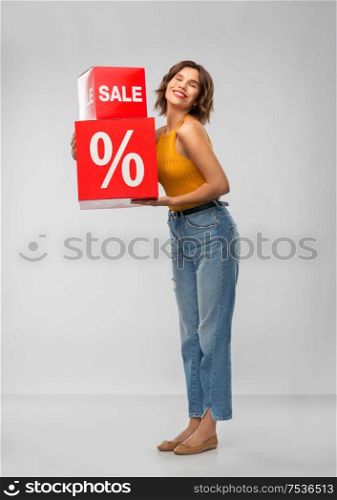 shopping, consumerism and people concept - happy smiling young woman in mustard yellow top and jeans with sale signs over grey background. happy smiling young woman with sale signs