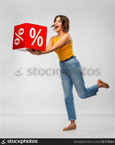 shopping, consumerism and people concept - happy smiling young woman in mustard yellow top and jeans with sale sign over grey background. happy smiling young woman with sale sign