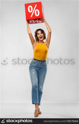 shopping, consumerism and people concept - happy smiling young woman in mustard yellow top and jeans with sale sign over grey background. happy smiling young woman with sale sign