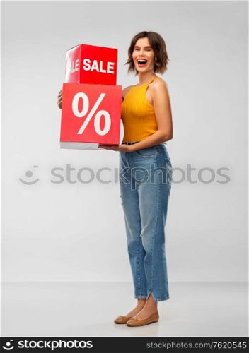shopping, consumerism and people concept - happy smiling young woman in mustard yellow top and jeans with sale signs over grey background. happy smiling young woman with sale signs