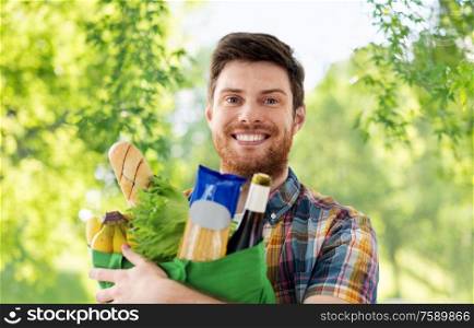shopping, consumerism and people concept - smiling young man with food in bag over green natural background. smiling young man with food in bag