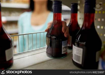 shopping, consumerism and people concept - woman taking bottle of vinegar or syrup from shelf at grocery