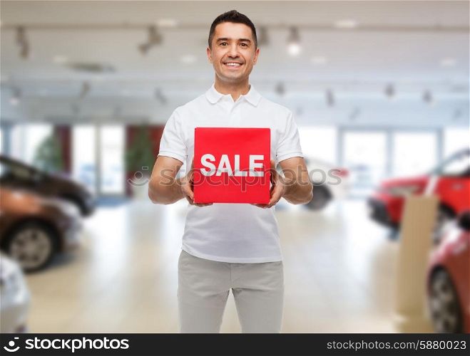 shopping, consumerism, discount and people concept - smiling man with red sale sigh over auto show background