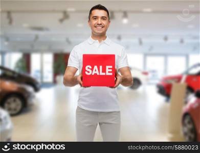 shopping, consumerism, discount and people concept - smiling man with red sale sigh over auto show background