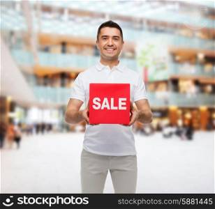 shopping, consumerism, discount and people concept - smiling man with red sale sign over mall background