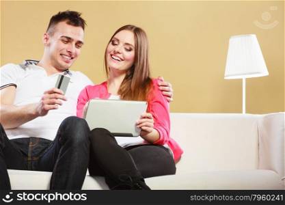 Shopping consumerism leisure and people concept. Young couple with tablet pc and credit card on sofe at home doing shopping on internet