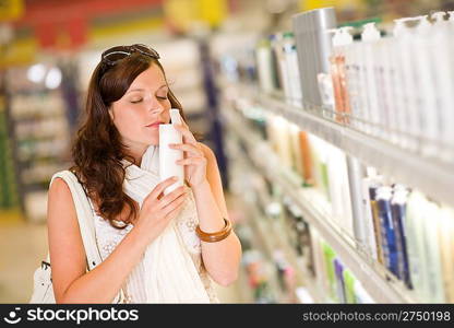 Shopping cosmetics - woman smelling bottle of shampoo in supermarket