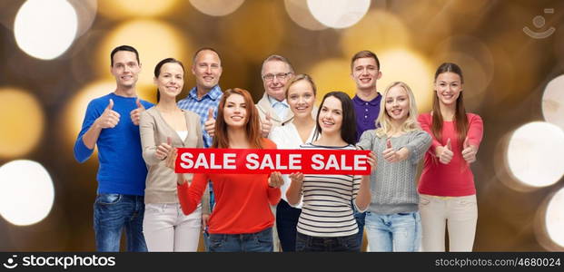 shopping, family, generation and people concept - group of happy men and women showing thumbs up and sale sign over holidays lights background