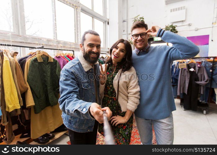 shopping, fashion and people concept - happy smiling friends taking picture by selfie stick at vintage clothing store. friends taking selfie at vintage clothing store. friends taking selfie at vintage clothing store