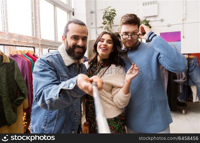 shopping, fashion and people concept - happy smiling friends taking picture by selfie stick at vintage clothing store. friends taking selfie at vintage clothing store