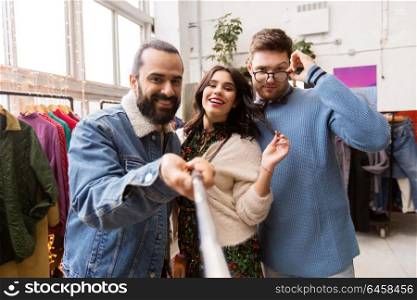 shopping, fashion and people concept - happy smiling friends taking picture by selfie stick at vintage clothing store. friends taking selfie at vintage clothing store