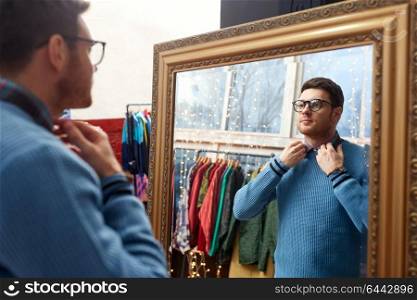 shopping, fashion and sale concept - man or hipster choosing clothes and looking at mirror at vintage clothing store. man looking at mirror at vintage clothing store