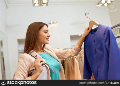 shopping, fashion, sale and people concept - happy young woman choosing clothes in mall or clothing store. happy woman choosing clothes at clothing store