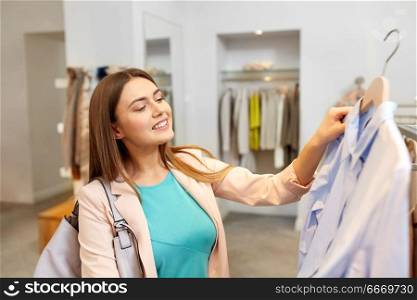 shopping, fashion, sale and people concept - happy young woman choosing shirt in mall or clothing store. happy woman choosing clothes at clothing store. happy woman choosing clothes at clothing store