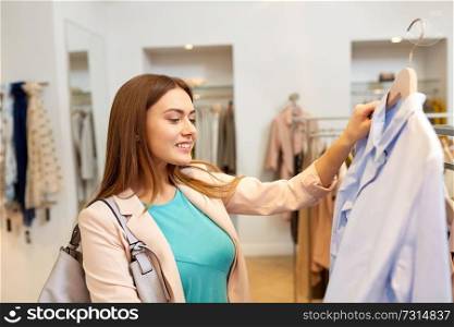 shopping, fashion, sale and people concept - happy young woman choosing shirt in mall or clothing store. happy woman choosing clothes at clothing store