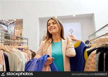 shopping, fashion, sale and people concept - happy young woman with clothes on hangers in mall or clothing store. happy young woman choosing clothes in mall